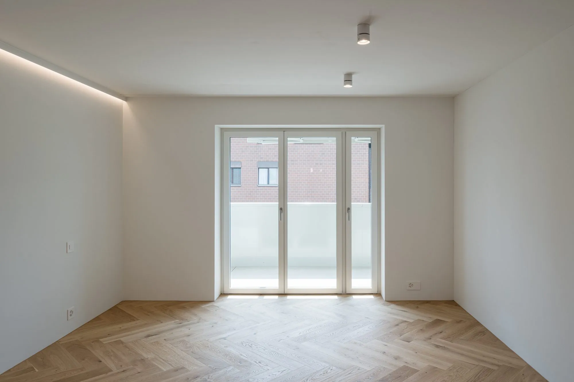 Zimmer mit Fenstertür zum Balkon, indirektem Deckenlicht und Eichenparkett