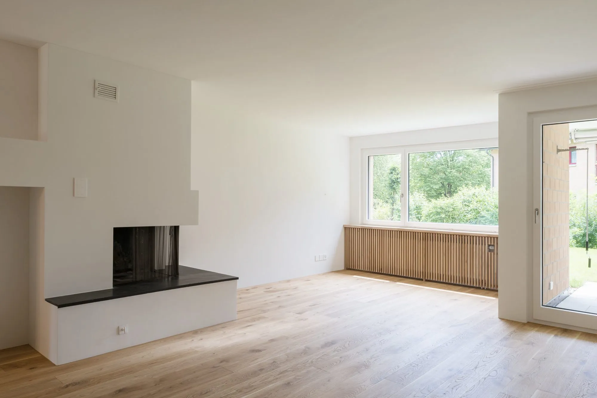 Wohnzimmer mit Cheminée, Eichenparkett und grossem Fenster ins Grüne